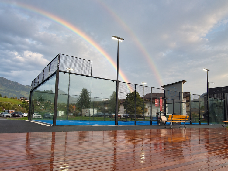 Ein nasser Padel-Court und im Himmel sieht man 2 Regenbogen