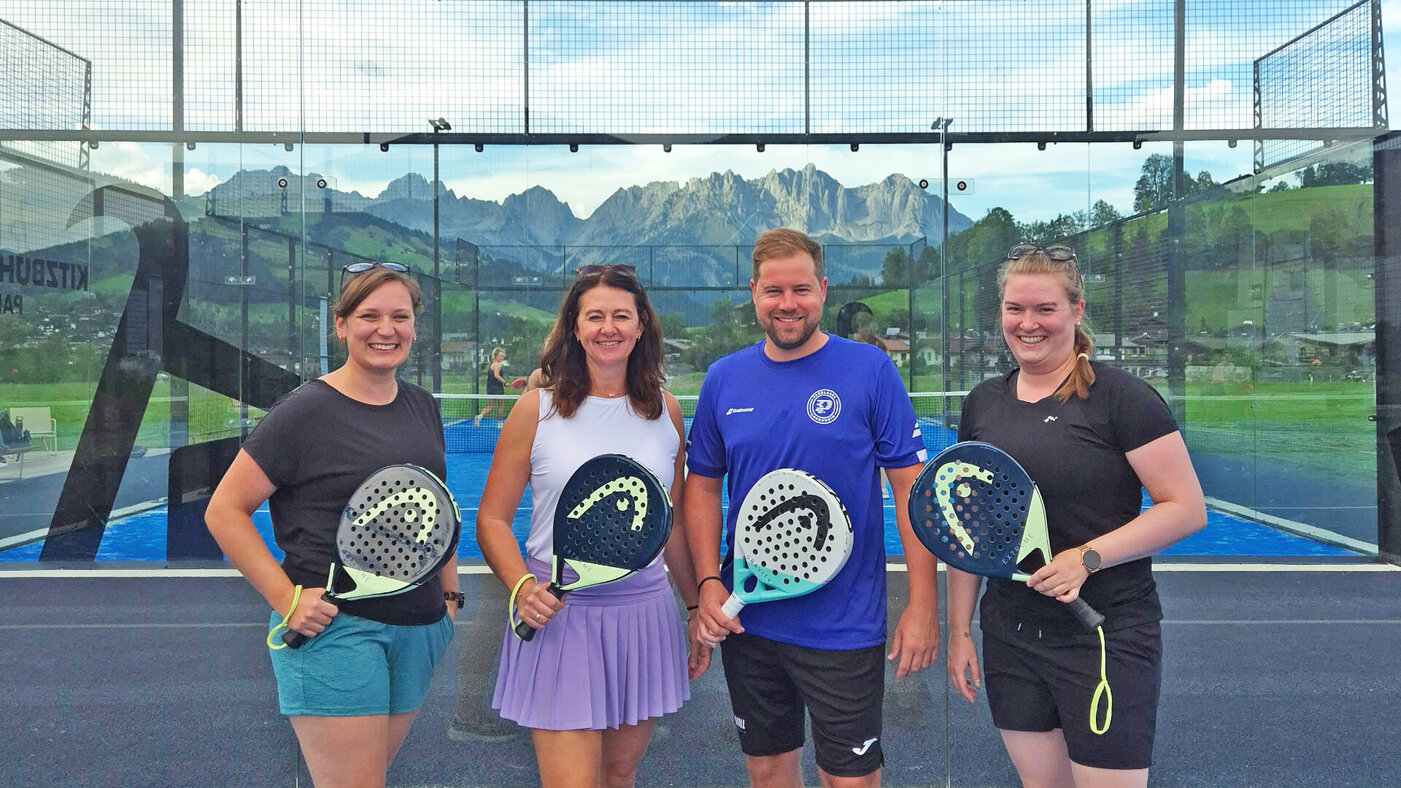 Vier Abteilungen, ein Court Ein Gruppenfoto mit 3 Frauen und einem Mann, alle haben Padel-Schläger in der Hand